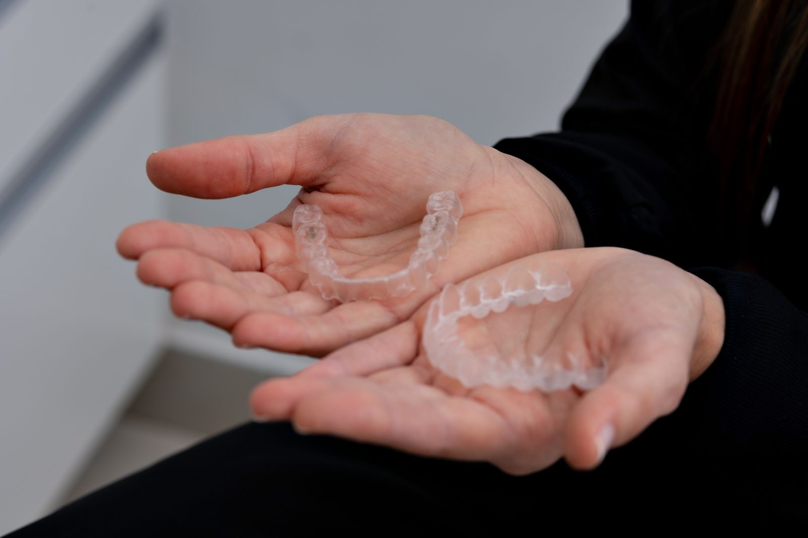 Duas mãos segurando alinhadores transparentes